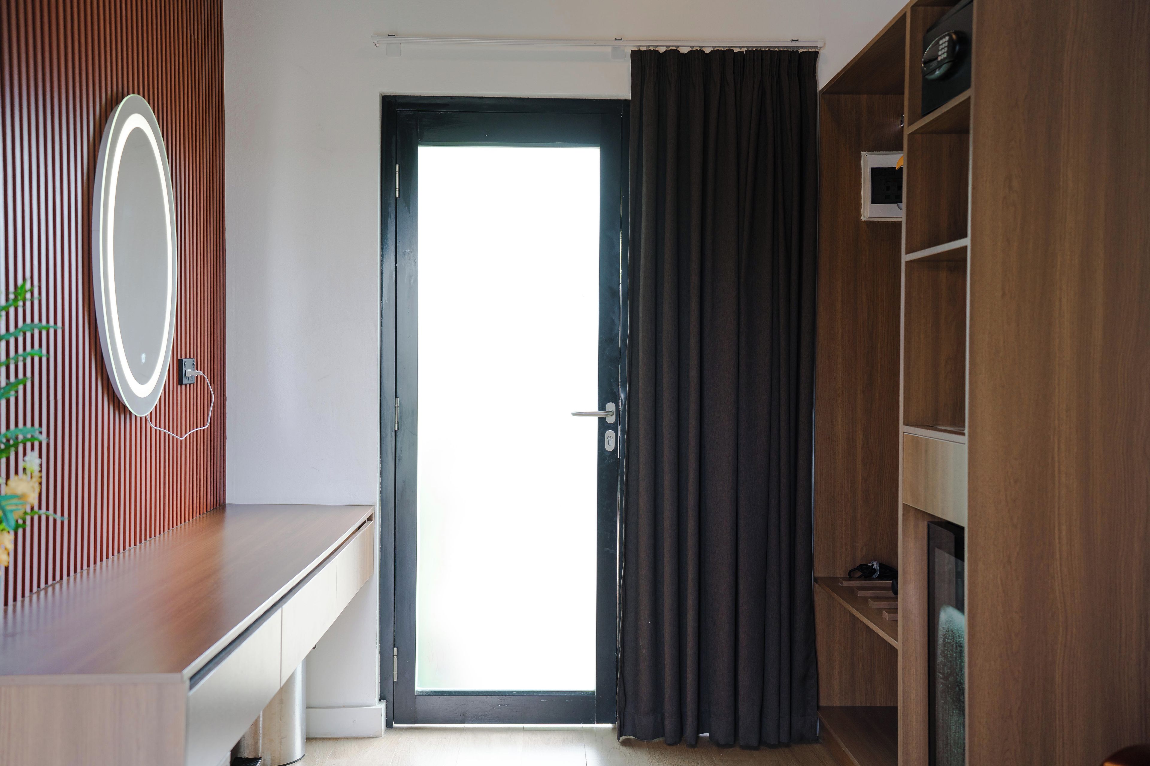 Une pièce avec un bureau en bois, un miroir, une porte avec des rideaux et une étagère intégrée.