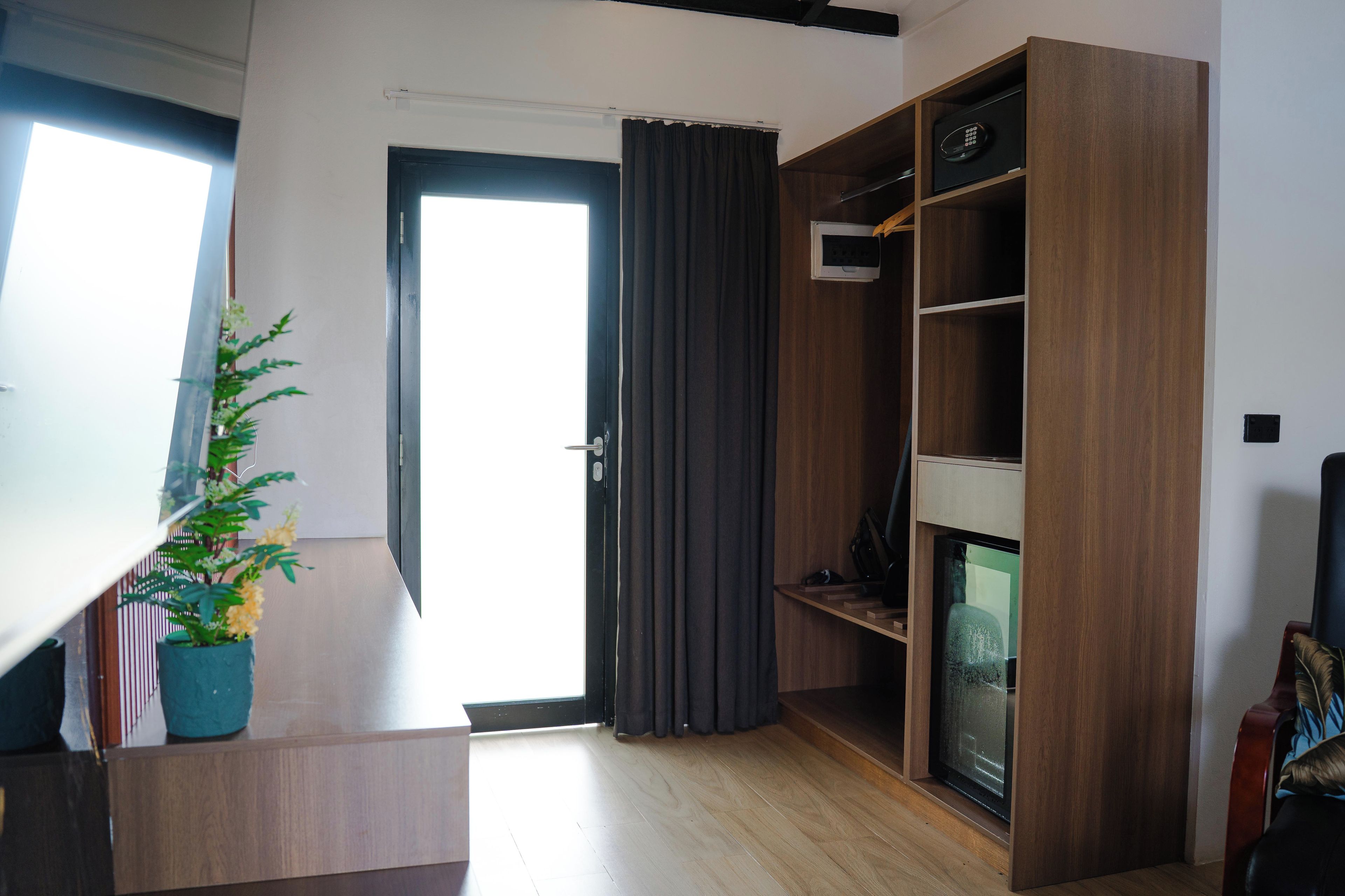 A modern living room with a wooden floor, a built-in TV, a potted plant, and a door leading to another room.