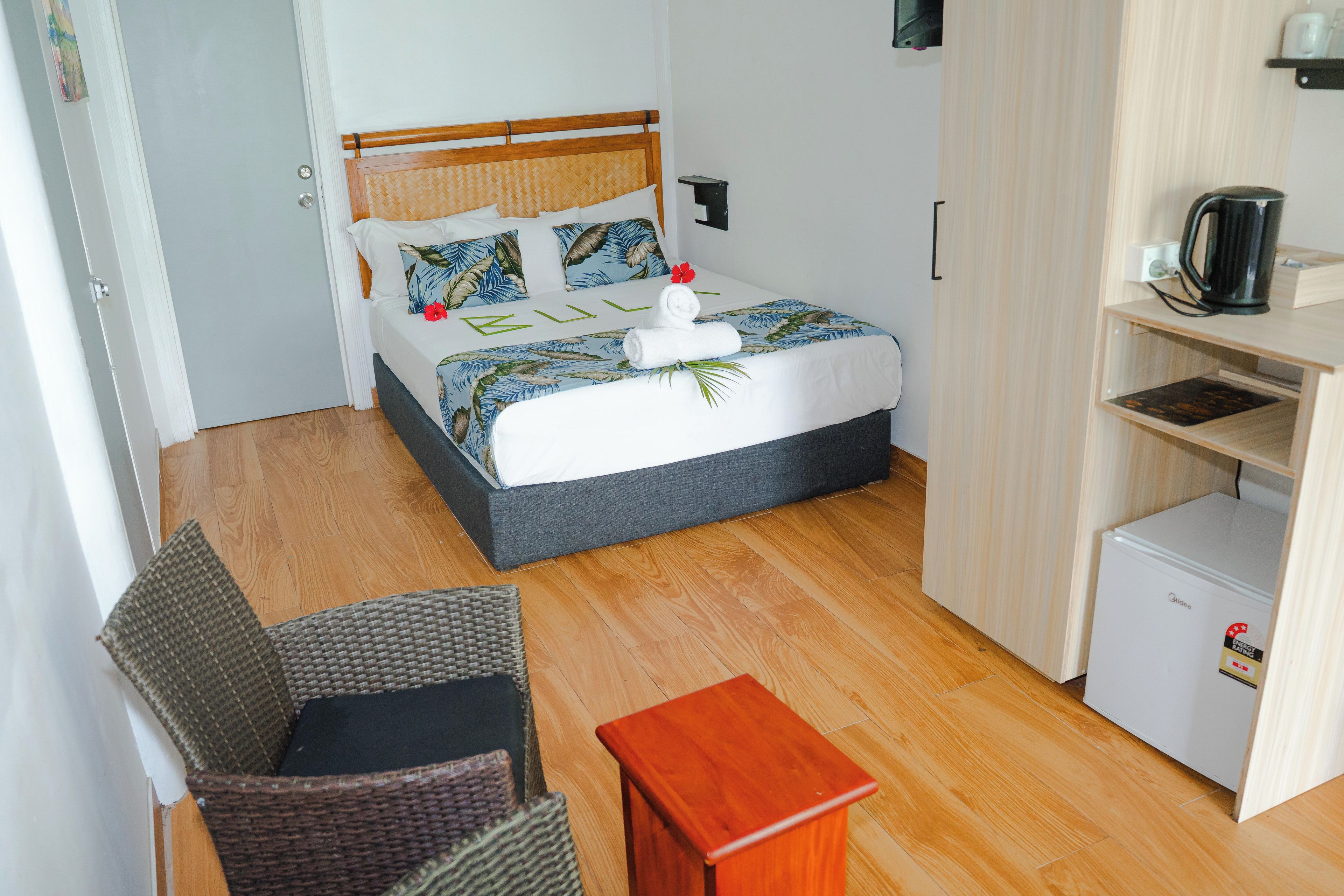 A hotel room with a bed, a small table, a chair, a kitchenette, and a door.