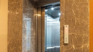 Egy márványfalú és -padlós lift, fém belsővel és egy gombbal ellátott kezelőpanellel.