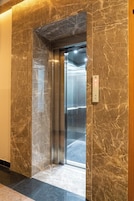 An elevator with a marble wall and floor, a metallic interior, and a control panel with a button.