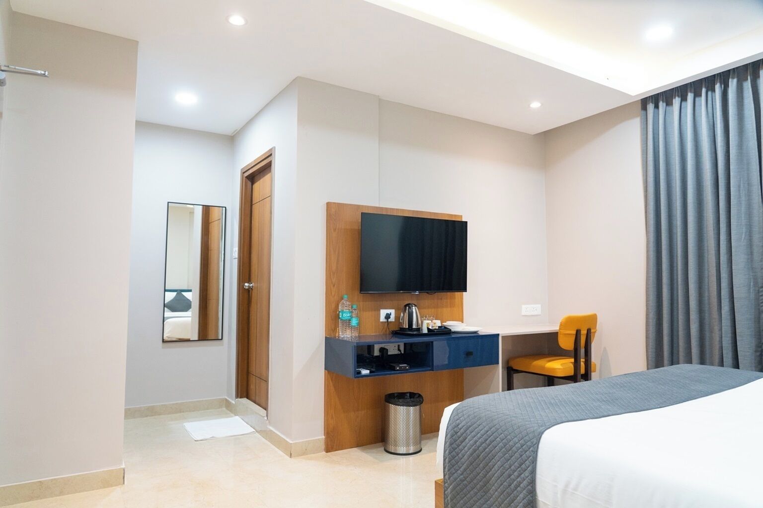 A hotel room with a bed, a desk with a flat-screen TV, a chair, and a large window with curtains.