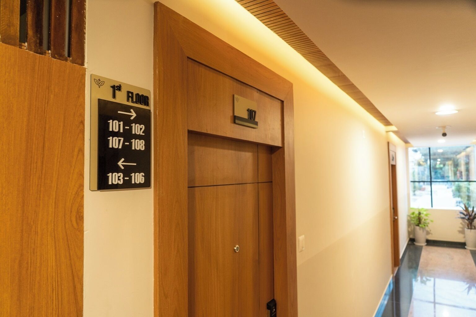 A hotel hallway with a wooden door and a sign indicating room numbers 101-102, 107-108, and 103-106.
