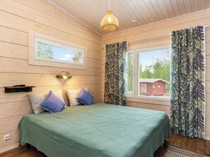 A room with a bed, a window with curtains, a hanging light fixture, and a small shelf. - Käpälämäki by Interhome (Hartola)