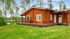A wooden cabin with a deck, a small porch, and a view of a lake.