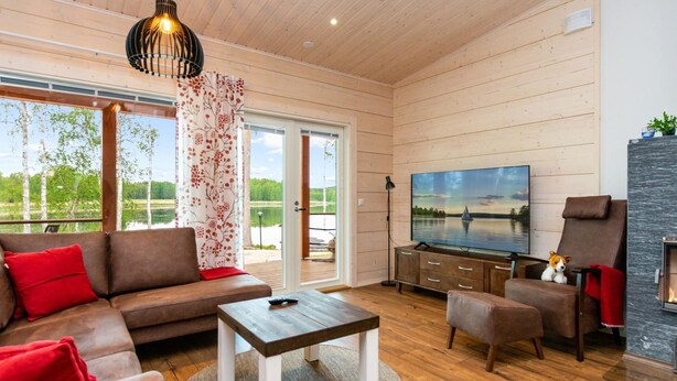 A spacious living room with a large TV, wooden flooring, a sofa, a coffee table, and a fireplace.
