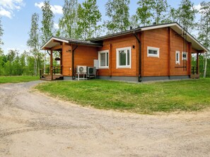 A wooden cabin with a porch, a gravel driveway, and a grassy area.