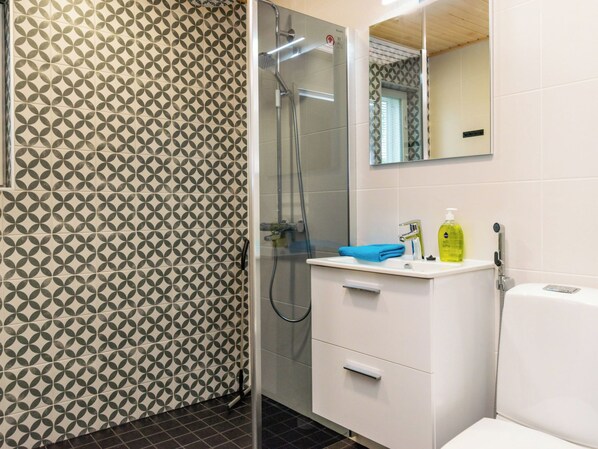A bathroom with a patterned wall, a glass-enclosed shower, a white sink with a mirror, and toiletries.