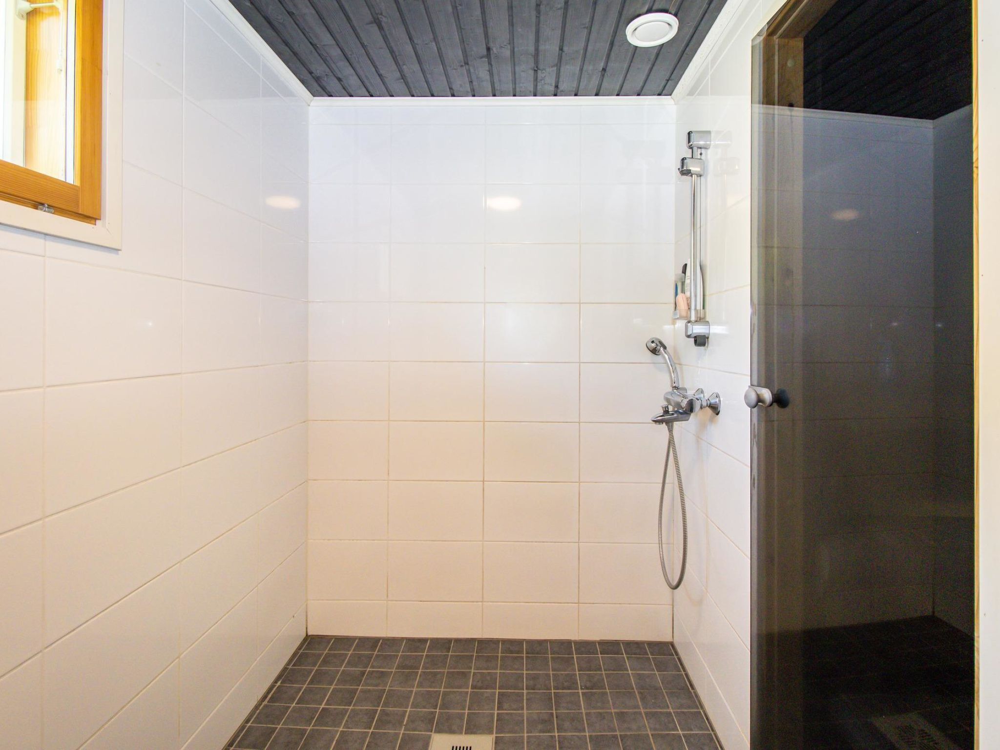 A small, tiled shower room with a glass door and a wooden ceiling.
