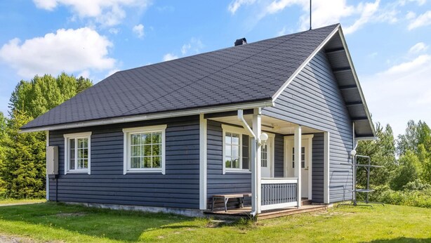 Uma casa térrea com fachada cinza escura, telhado em duas águas e varanda coberta com um banco.