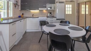 Cozinha moderna com armários brancos, micro-ondas, fogão e pia. Há uma mesa de jantar com cadeiras pretas e uma janela com cortinas.