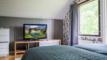 Makuuhuoneessa on televisio puisen jalustan päällä, kaksi tummilla tekstiileillä varustettua sänkyä, valkoinen lipasto ja ikkuna, josta avautuu näkymä vehreään maisemaan.