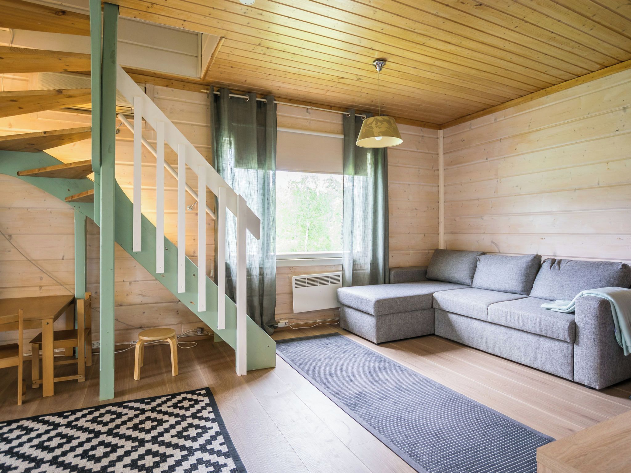 Un interno in legno con una scala, un divano grigio e un tappeto decorato.