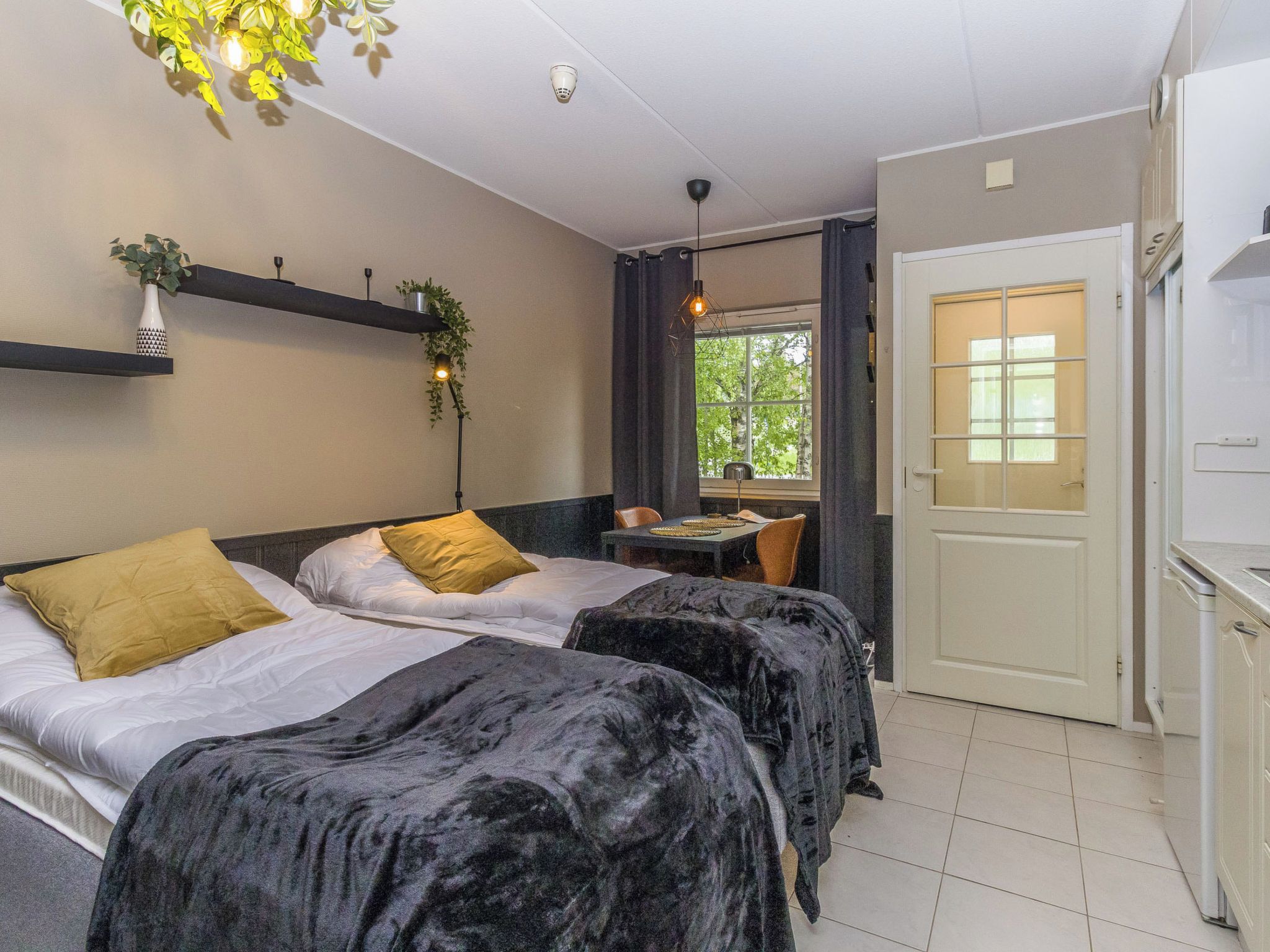 A room with two beds, a dining table, and a window with a view of trees.
