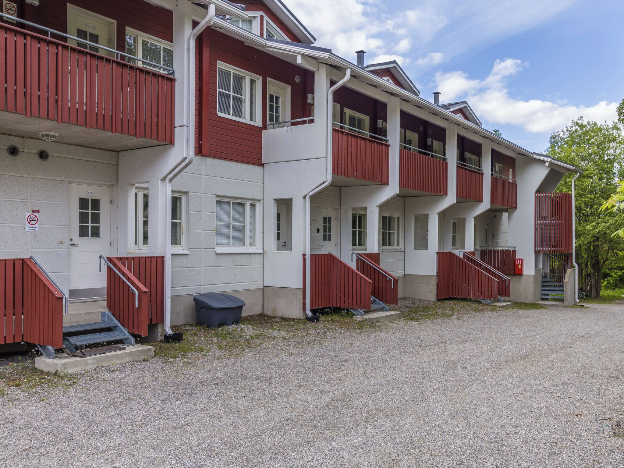 A multi-story building with balconies, a gravel driveway, and a clear sky.