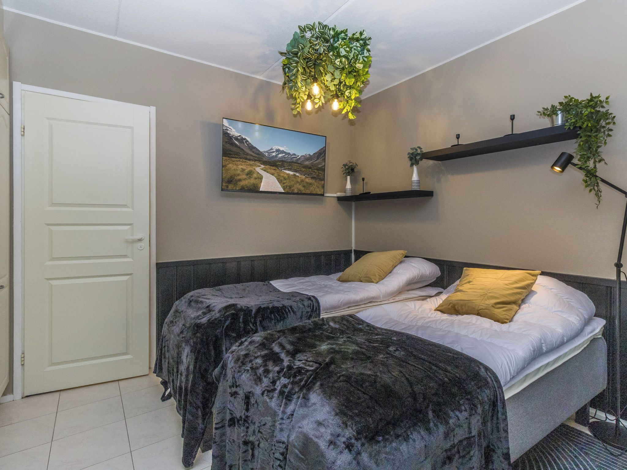 Un dormitorio con cama, una puerta, televisor montado en la pared y una planta colgante.