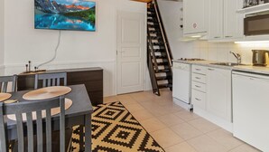 A modern kitchen with white cabinets, a built-in microwave, and a coffee maker. There is a dining area with a table and chairs, and a staircase leading to an upper level. - Levin lumi by Interhome (Kittilä)