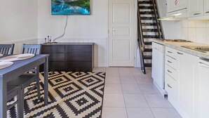 A modern kitchen with white cabinets, a black and white patterned rug, a dining area with a table and chairs, and a painting of a mountain landscape on the wall. - Levin lumi by Interhome (Kittilä)