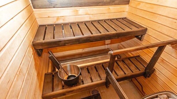A sauna with wooden benches, a metal basin, and a container of stones. - Levin lumi by Interhome (Kittilä)