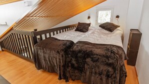 A bedroom with a sloped ceiling, a bed with dark bedding, a wooden floor, and a window with a view of greenery. - Levin lumi by Interhome (Kittilä)