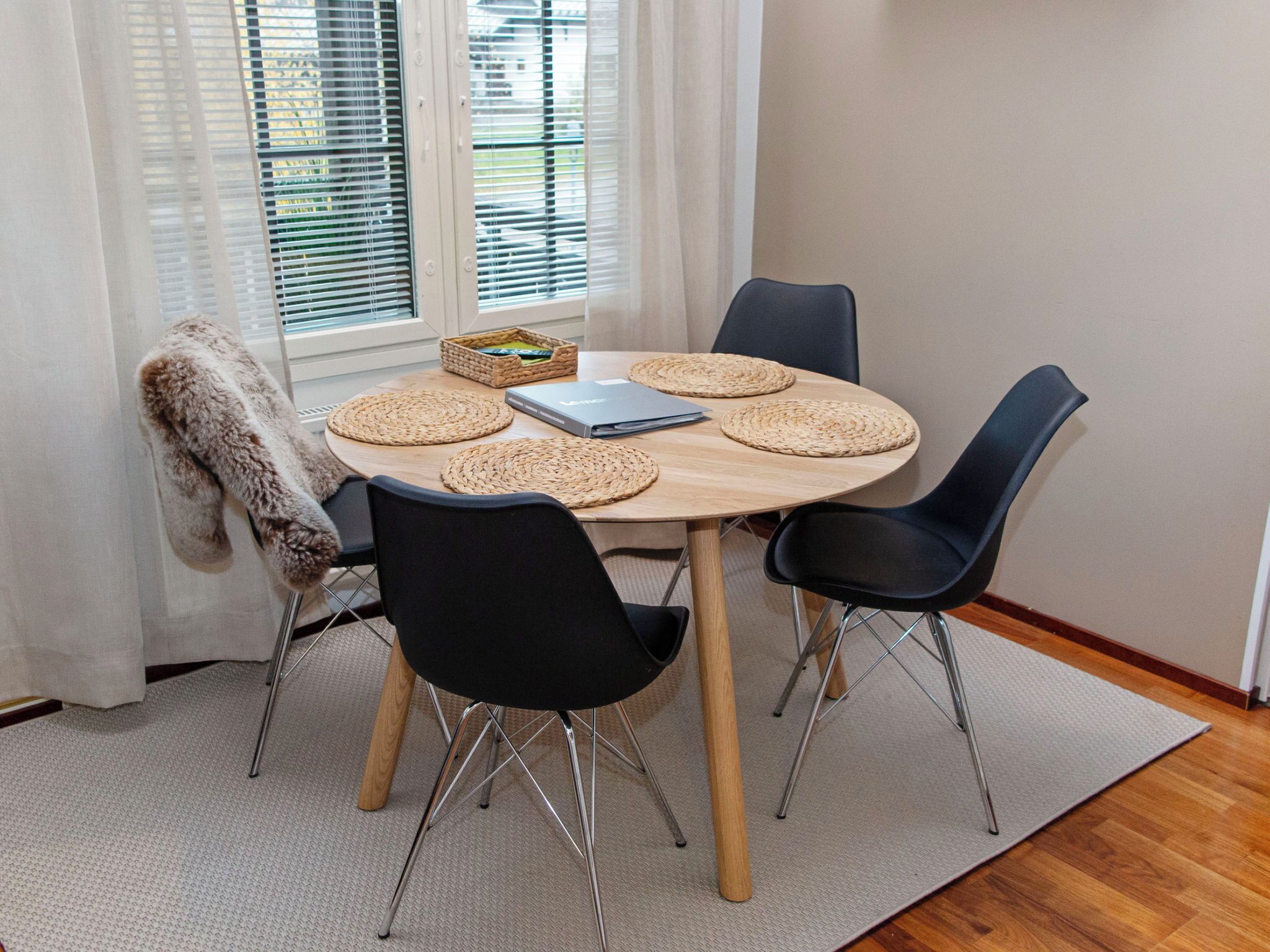 A round wooden table with four black chairs, a laptop, and woven placemats.