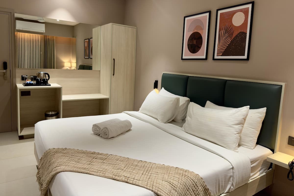 A hotel room with a bed, a desk, a wardrobe, and two framed artworks on the wall.