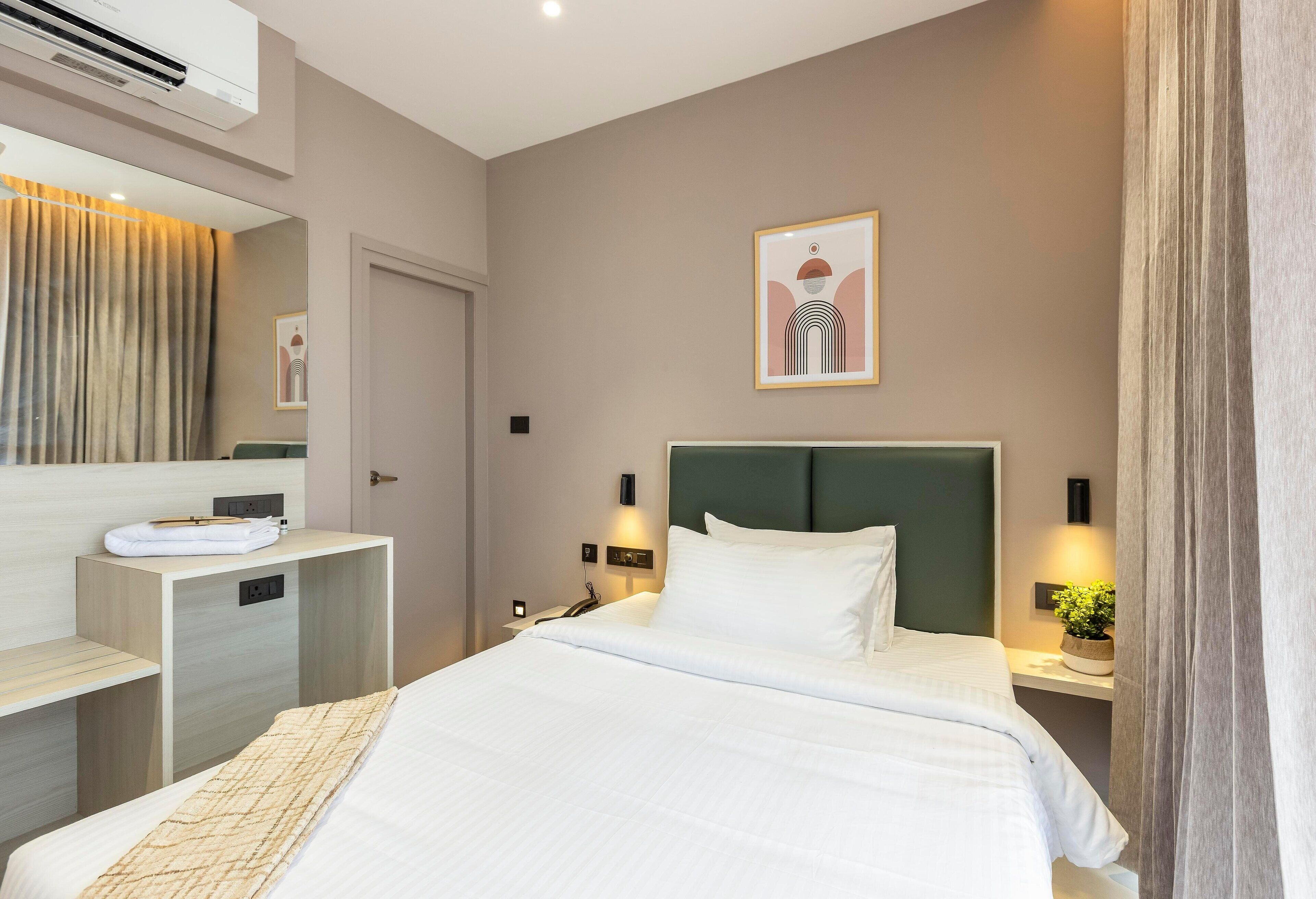 Une chambre d’hôtel comprenant un lit, une table de chevet, une commode, un climatiseur fixé au mur et un tableau encadré accroché au mur.