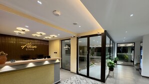 Un hall d'accueil moderne avec un comptoir de réception, une enseigne indiquant « Altin STAYS » et une porte vitrée donnant accès à l'intérieur.