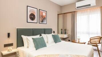 A modern hotel room with a large bed, a bedside table, a chair, and artwork on the wall.