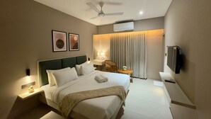 Une chambre d’hôtel moderne dotée d’un grand lit, d’un ventilateur de plafond, d’un téléviseur à écran plat et d’une petite table avec une lampe.