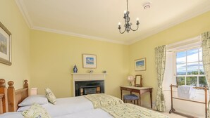 A bedroom with two beds, a fireplace, a desk with a chair, and a window with curtains.