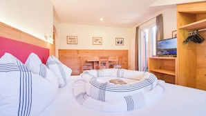 Un dormitorio acogedor con una cama redonda, cabecera de madera, televisión y estante de madera con ropa.