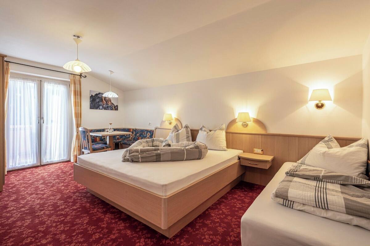 Habitación de hotel con una cama grande, una cama más pequeña, un escritorio con silla, un banco y un área de comedor.