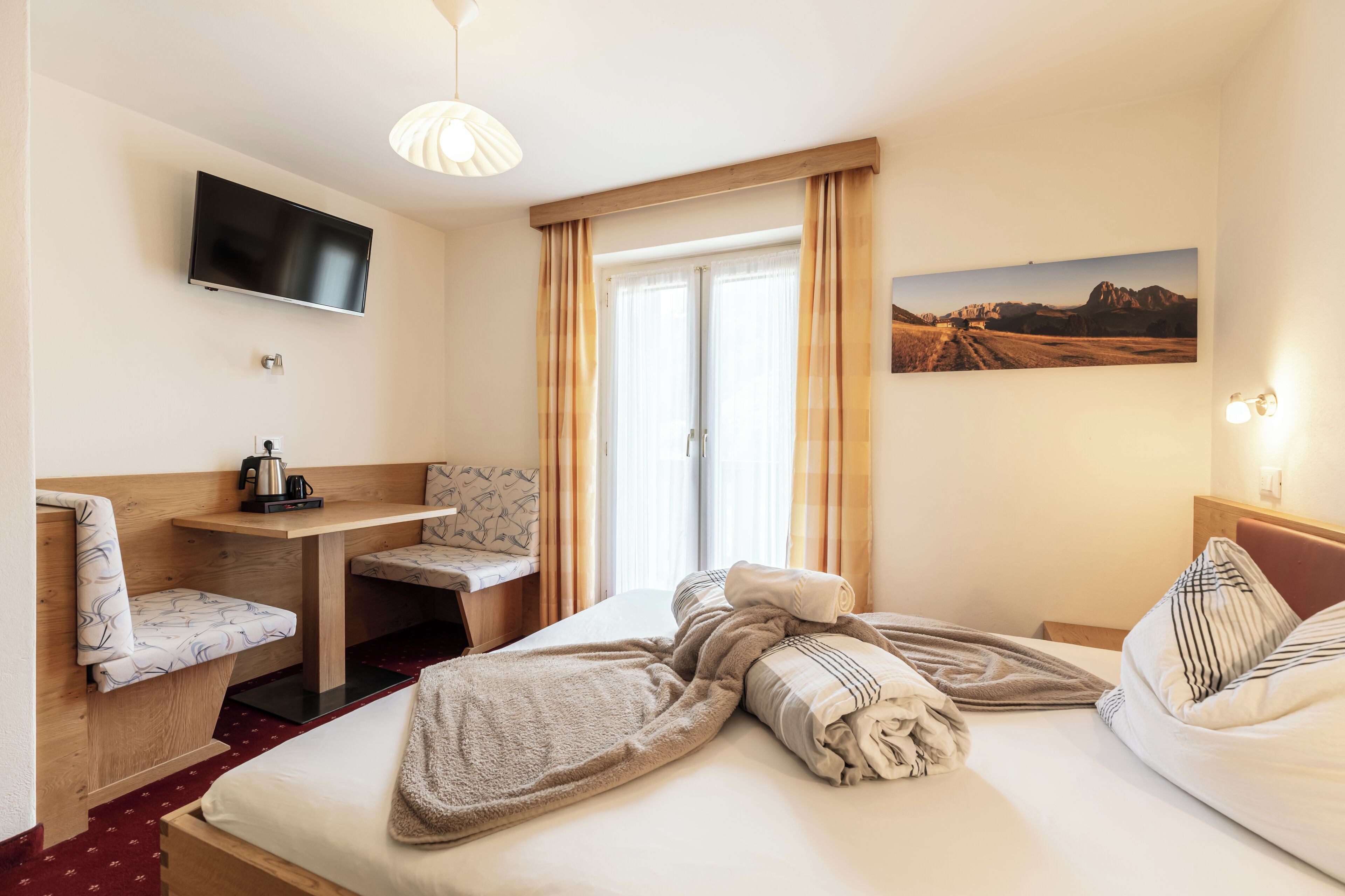 A hotel room with a bed, a desk, a chair, a TV, and a window with curtains.