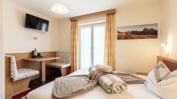 A hotel room with a bed, a desk, a chair, a TV, and a window with curtains.