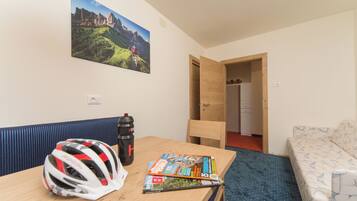 Quarto de hotel com mesa de madeira, uma revista, um capacete, garrafa de água, sofá e um quadro na parede.