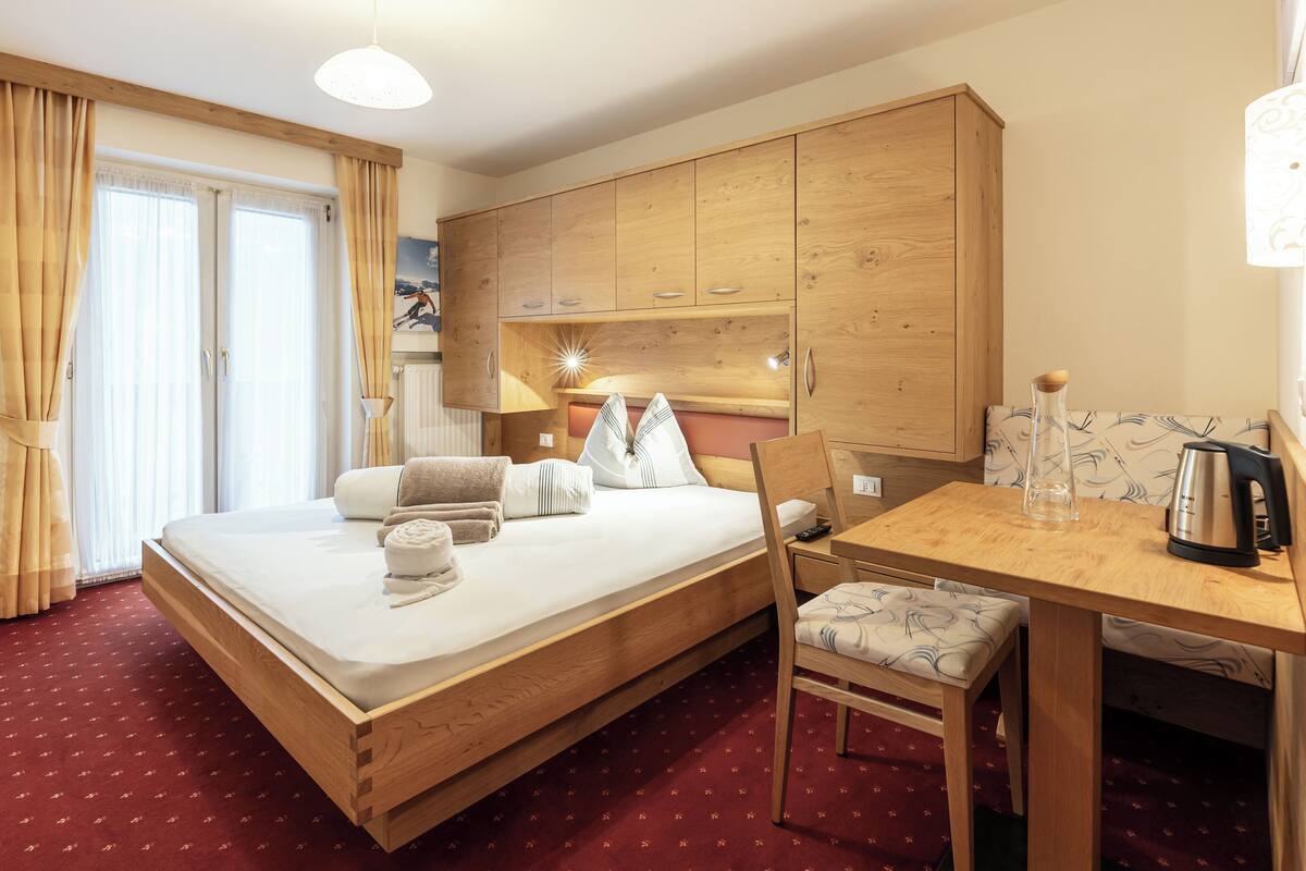 Una habitación de hotel con una cama de madera, una mesita, una silla y una zona de kitchenette.