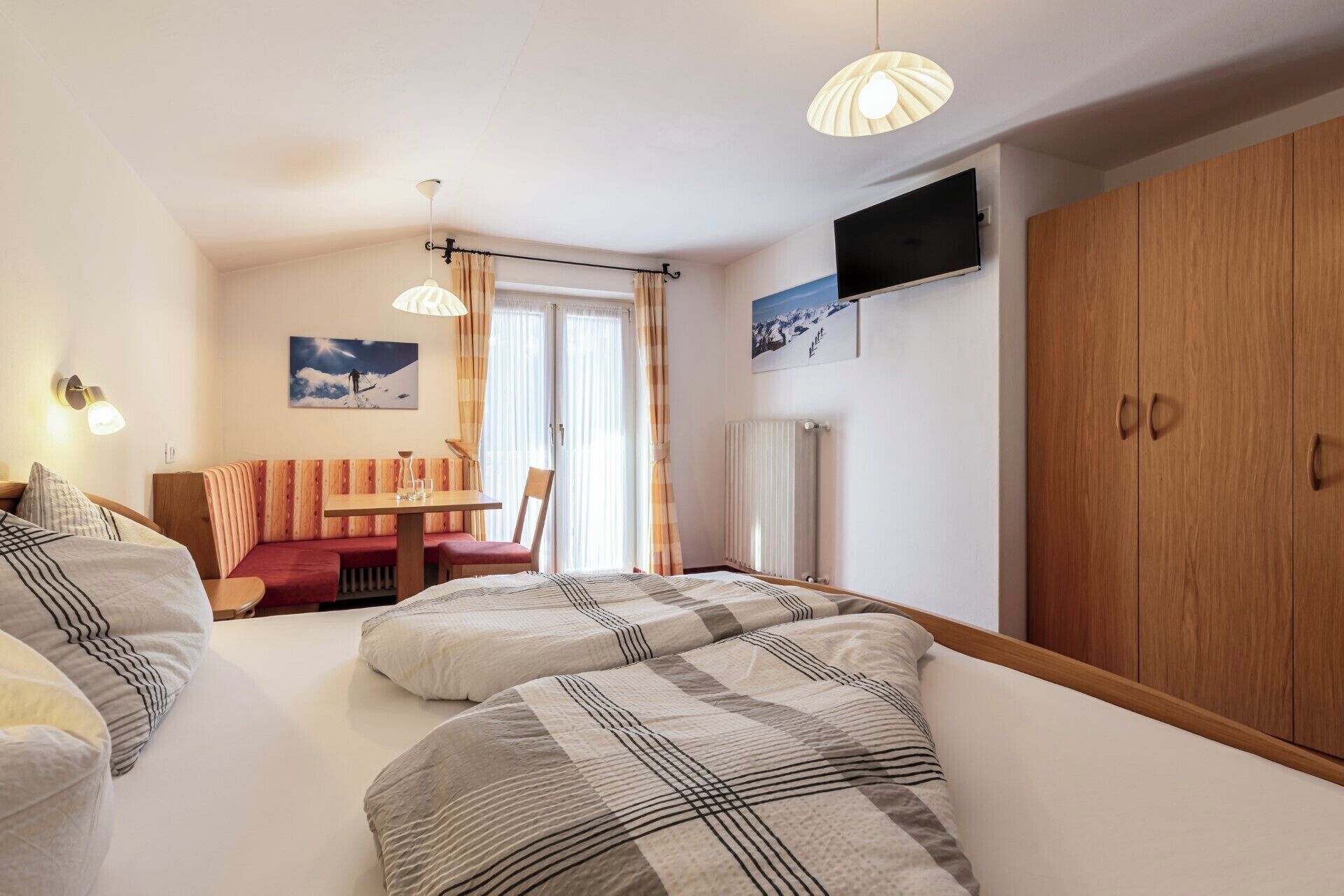 A bedroom with two beds, a wooden wardrobe, a television, and a dining area with a table and chairs.