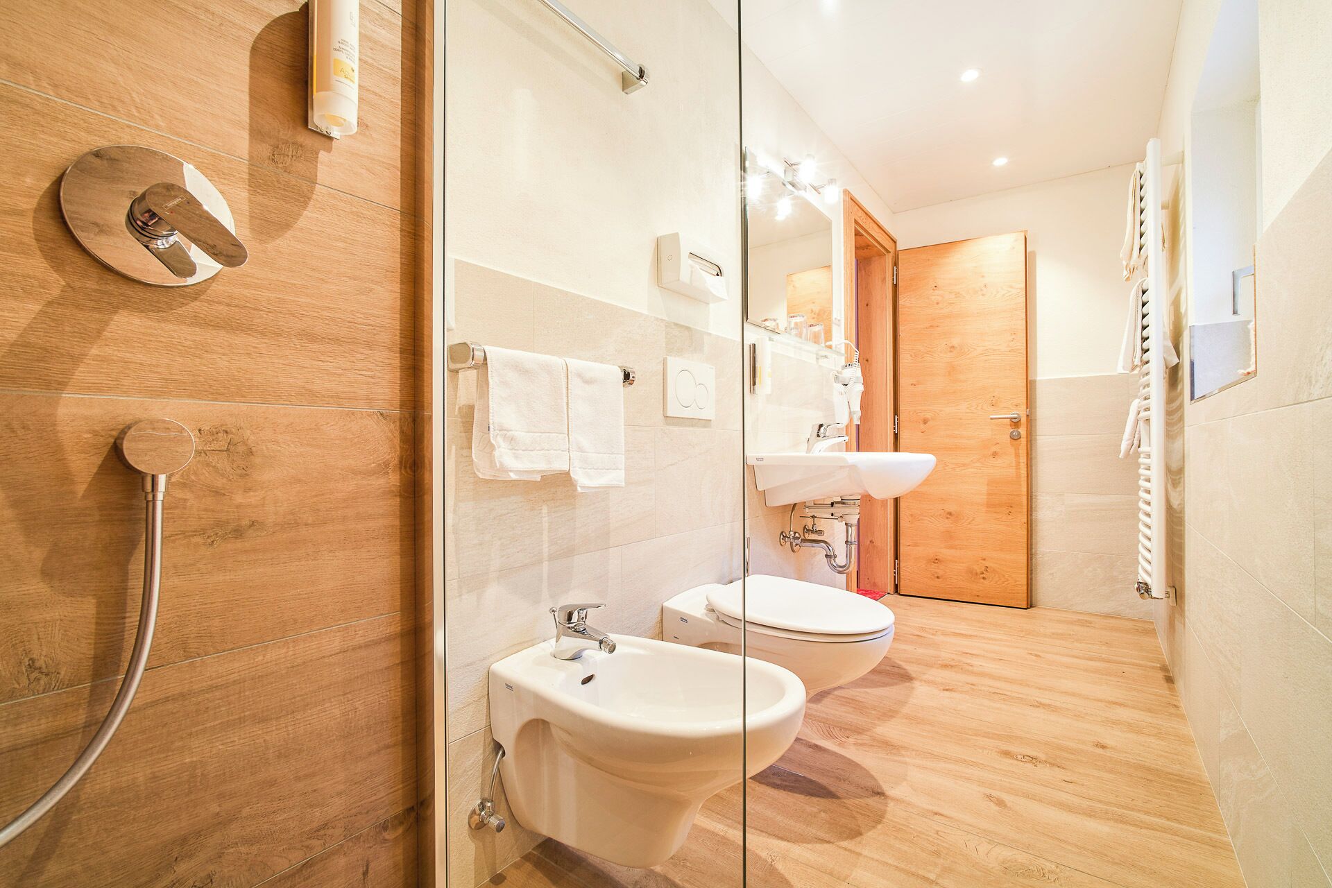 Een moderne badkamer met een douchecabine van glas, een bidet, toilet en wastafel.