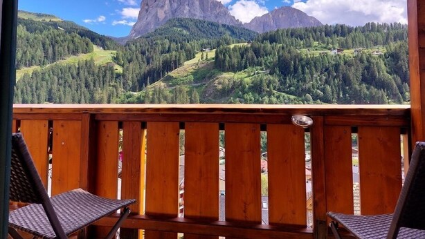 Una terraza de madera con dos sillas de mimbre mirando un paisaje montañoso con un pico destacado.