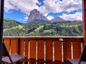 Une terrasse en bois avec deux fauteuils en osier donnant sur un paysage montagneux, avec un sommet particulièrement imposant.