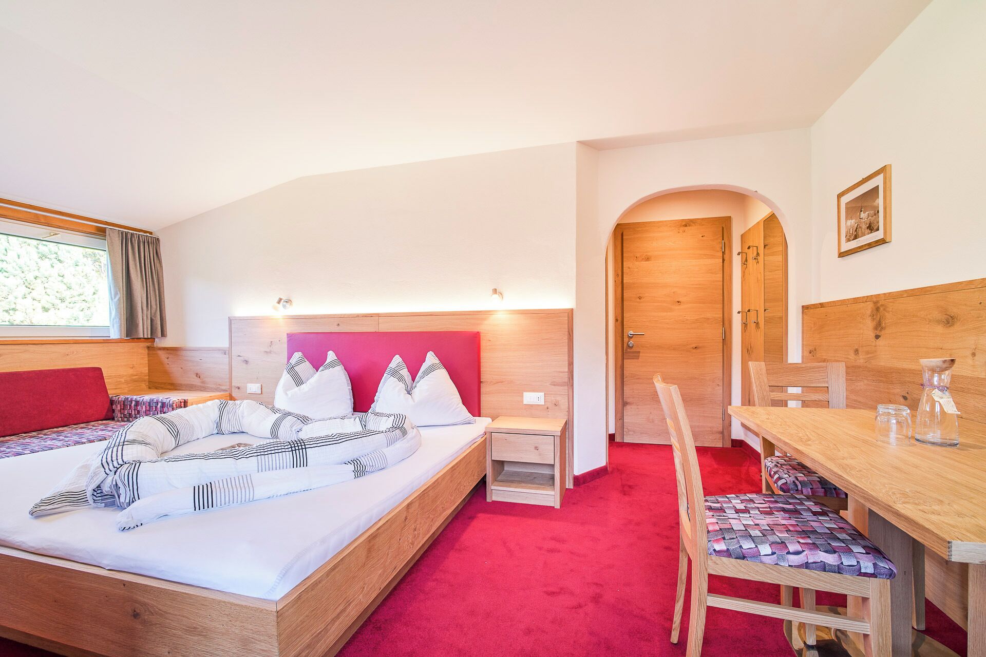 Una camera da letto con un letto in legno, un tappeto rosso, una scrivania in legno e una sedia.