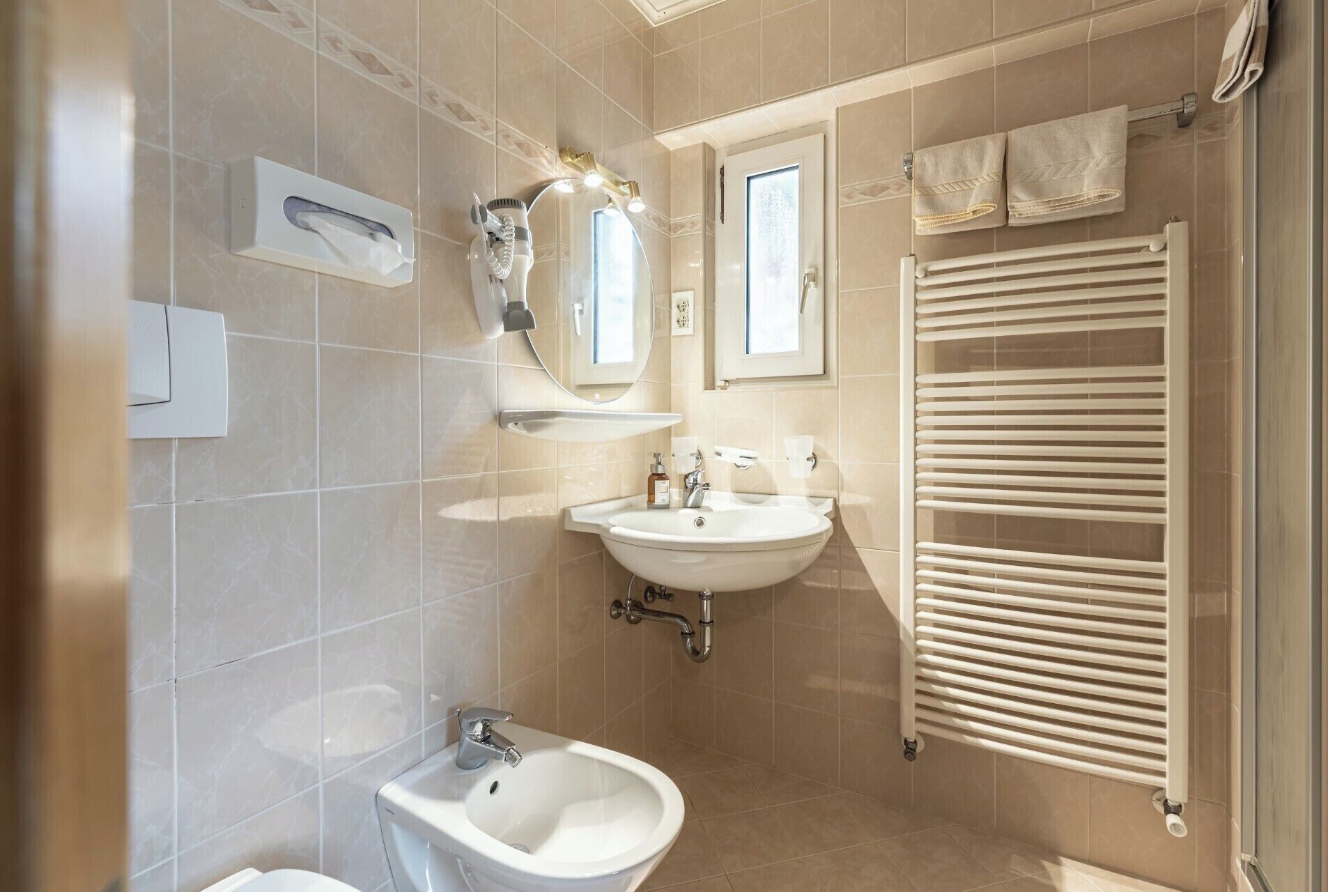 A modern bathroom with a bidet, sink, mirror, towel rack, and a radiator.