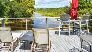 A deck with outdoor seating, including chairs and a table, overlooking a water body and surrounded by greenery. - Withlacoochee River Retreat w/ Dock: Paddle & Fish (Dunnellon)
