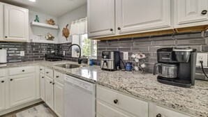 A modern kitchen with white cabinetry, granite countertops, and stainless steel appliances including a Keurig coffee maker. - Withlacoochee River Retreat w/ Dock: Paddle & Fish (Dunnellon)