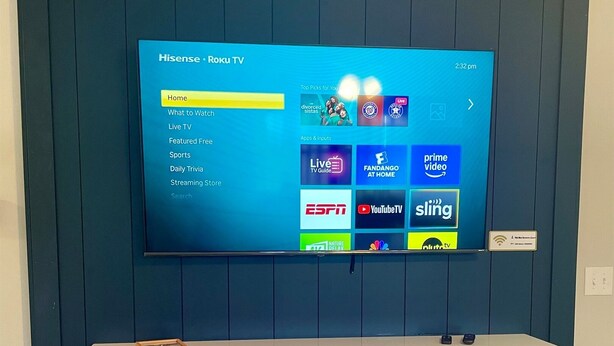A Hisense Roku TV mounted on a dark blue wall with a white entertainment unit below it.