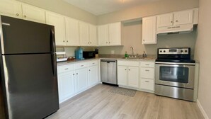 A modern kitchen with white cabinets, stainless steel appliances, and a light wood floor.