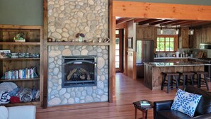 Una chimenea de piedra, estantes de madera, un sofá de cuero y una cocina con armarios de madera y una barra.