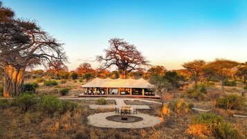 Un lodge de safari doté d’un espace de restauration en plein air, entouré d’un paysage naturel et d’arbres.
