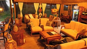 Un área de descanso al aire libre con carpas, asientos, una mesa y un refrigerador.